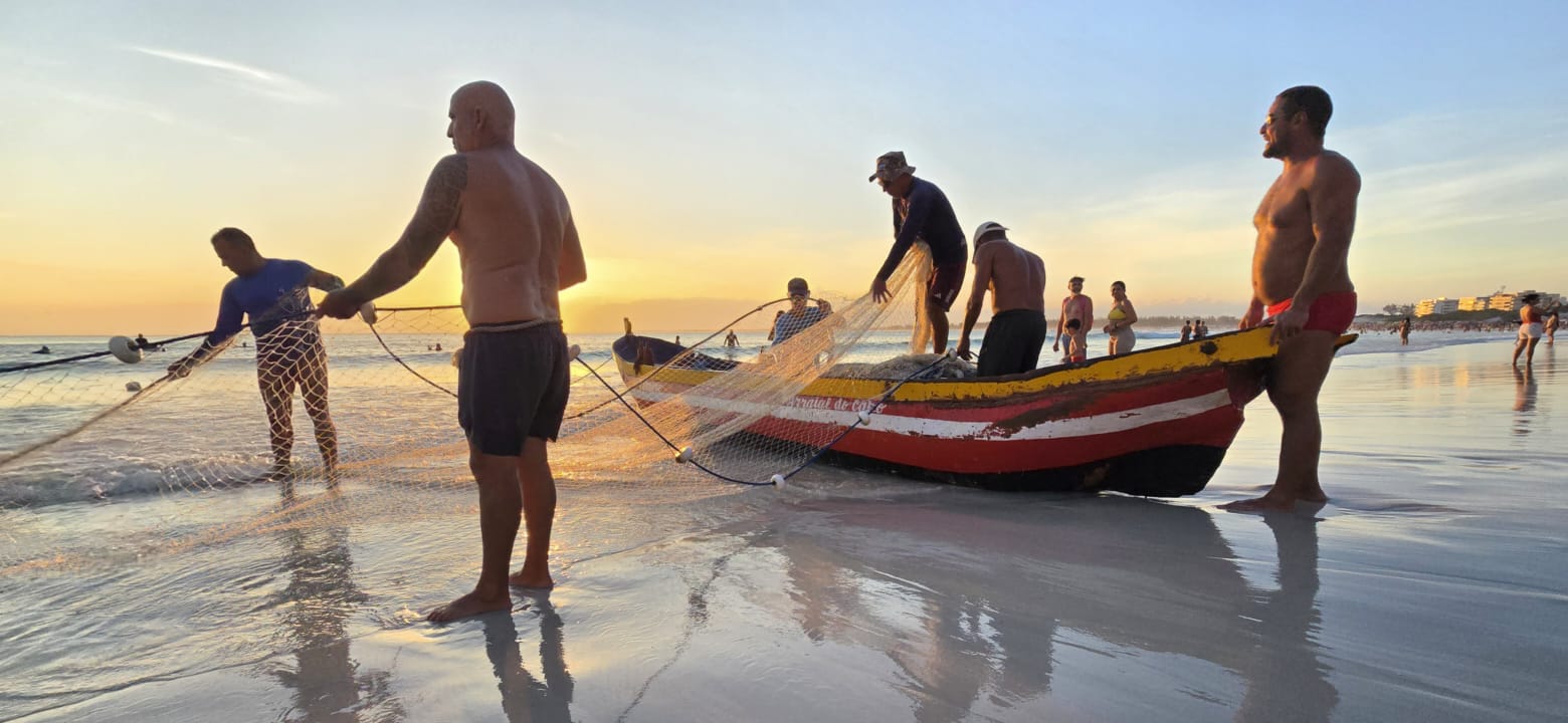 Pescadores artesanais puxam uma rede na praia ao pôr do sol