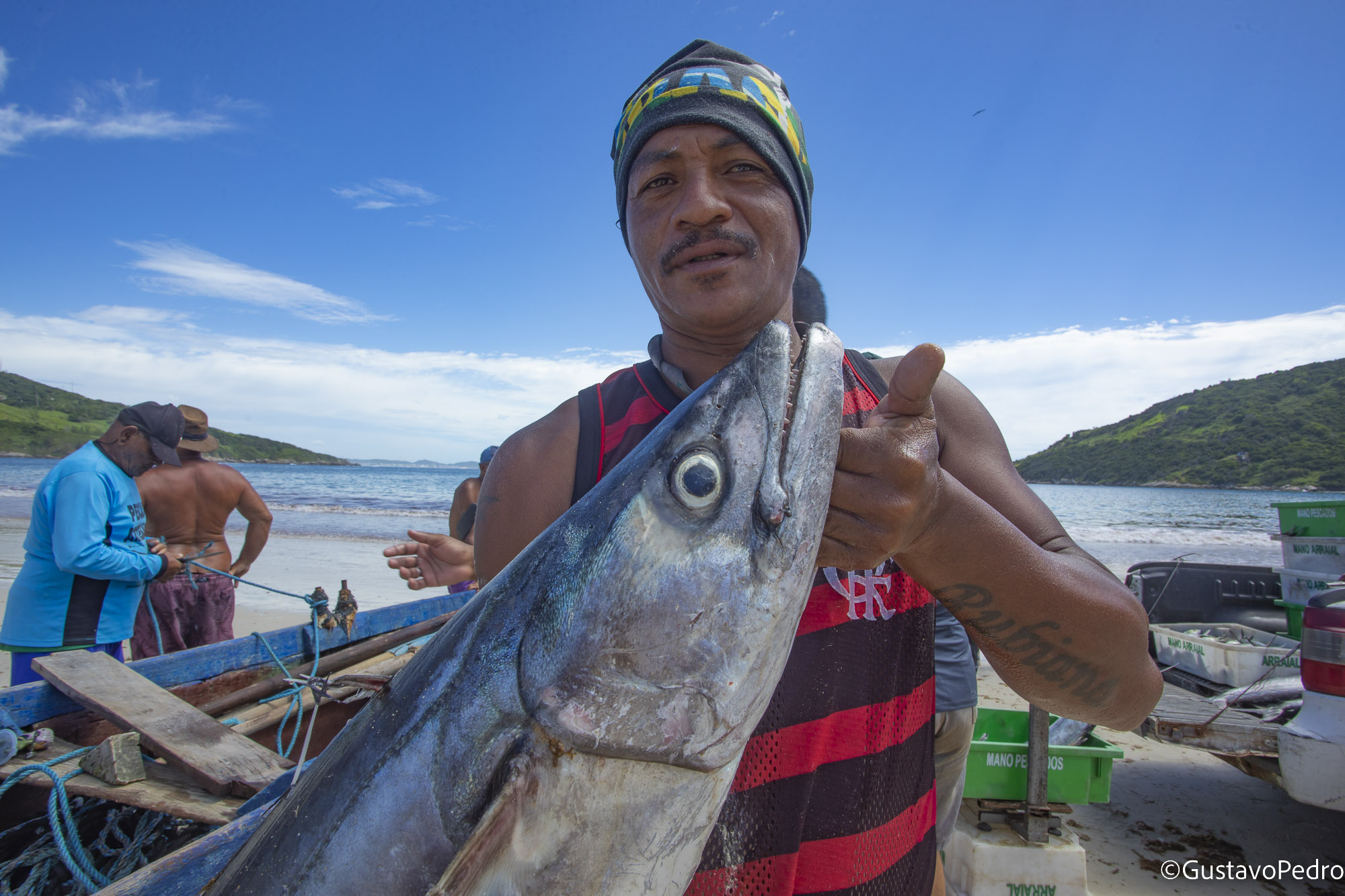 Pescador apresenta um peixe diante do mar e dos barcos de Arraial do Cabo