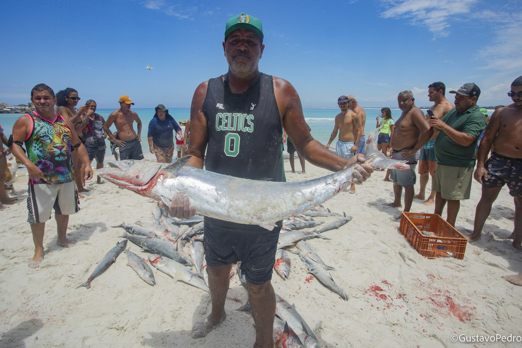Pescador apresenta um peixe junto à comunidade na praia