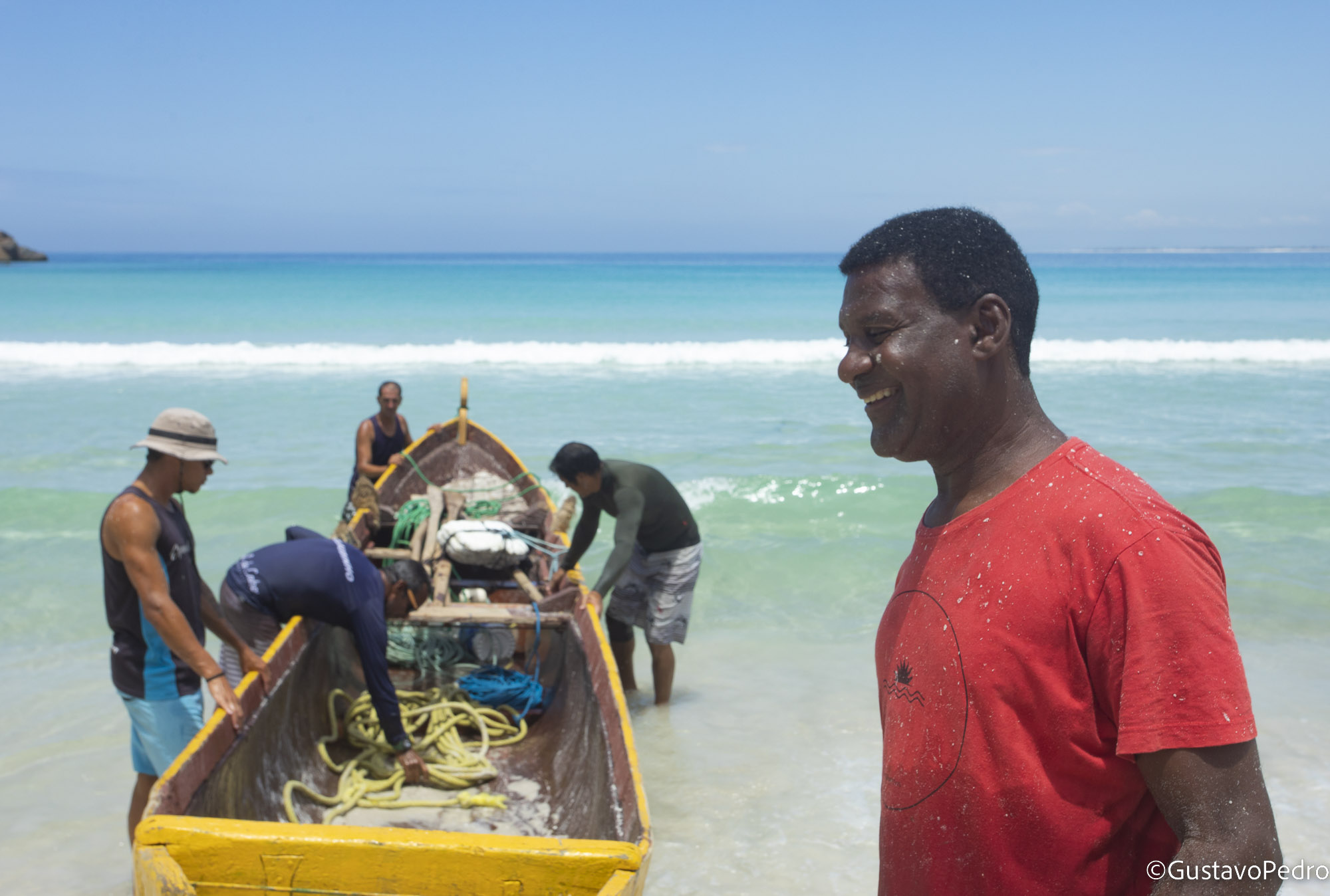 Pescador sorrindo ao lado de um barco artesanal na praia